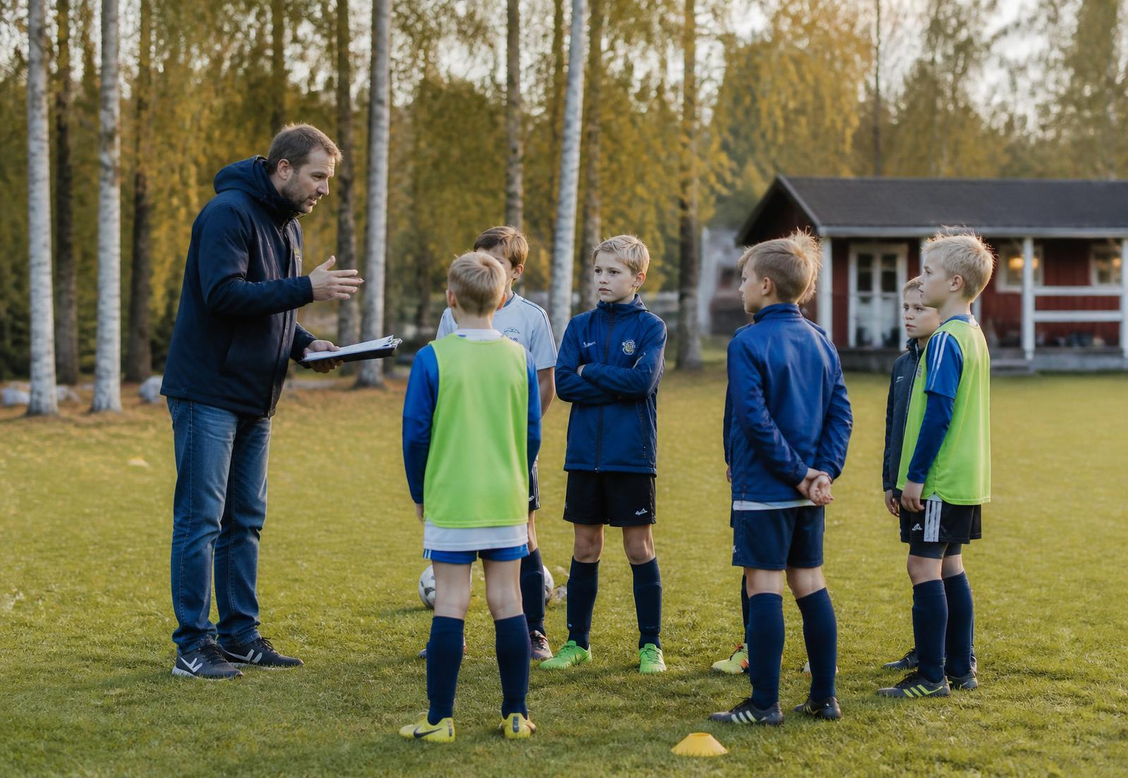 Ungdomslag på fotbollsträning med ideell ledare på en lokal gräsplan